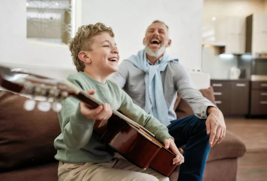 A grandfather and grandson share a joyful laugh during a music lesson, to illustrate Wise &Partner's experience serving the financial needs of multi-generations of families